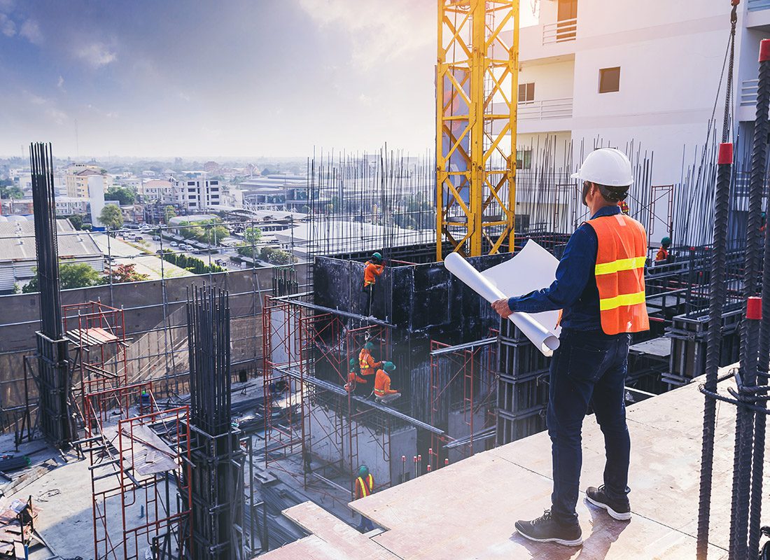 Insurance by Industry - An Engineer Stands on Top of a Platform While Holding Blueprints and Overseeing the Construction