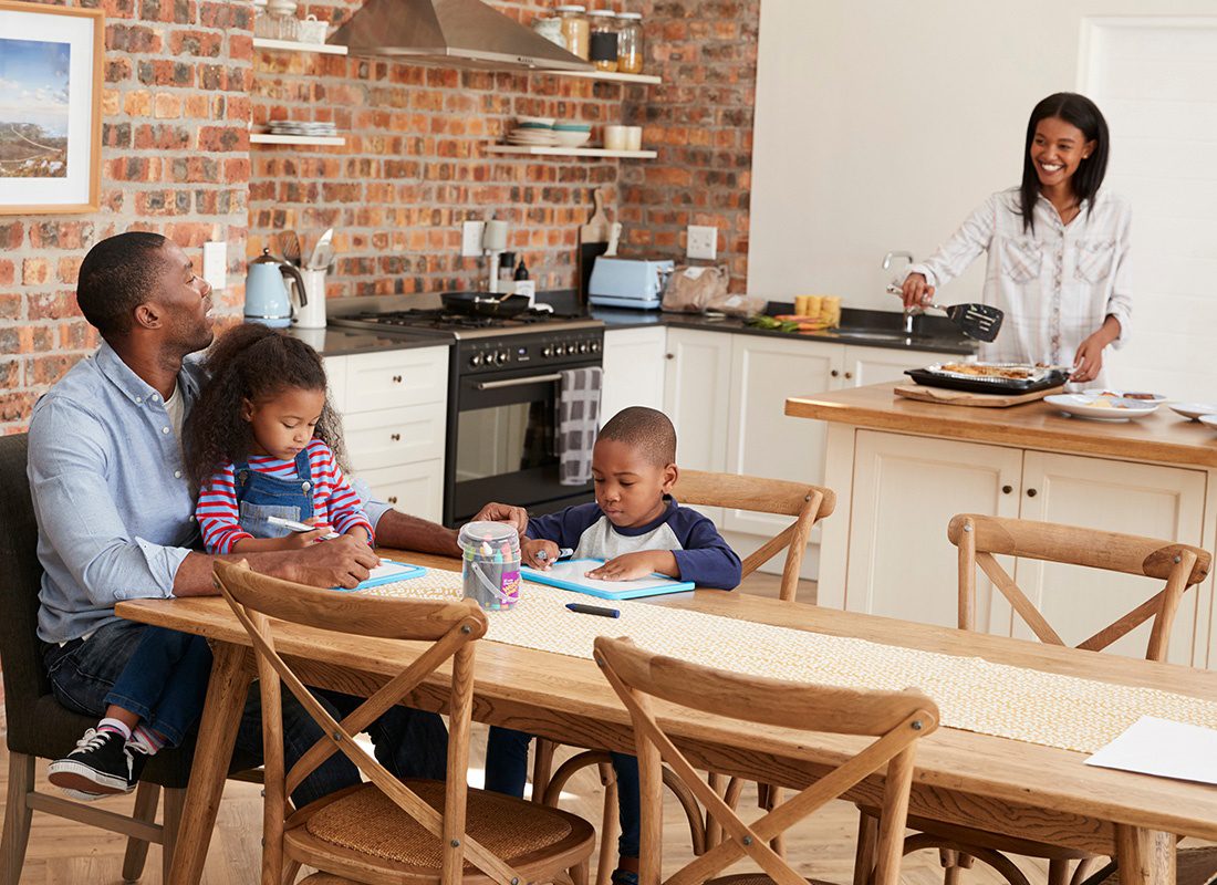Personal Insurance - Mother Smiles and Looks at Her Husband and Two Children as She Prepares Dinner and They Work on Coloring Drawings